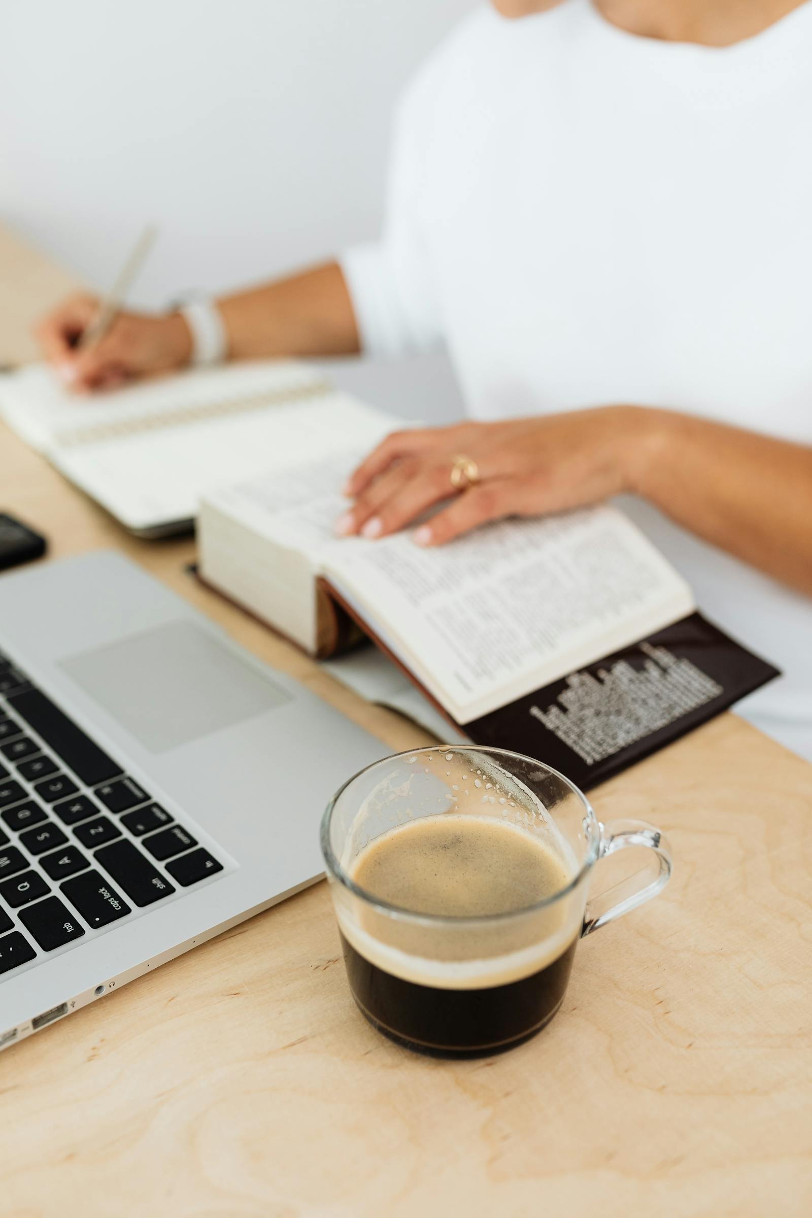 A woman writing in a journal at a desk with laptop and coffee.