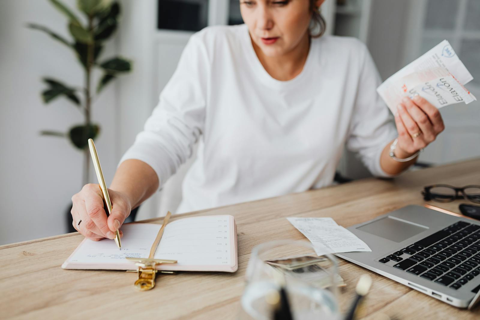 A woman writing in a planner with receipts and a laptop.